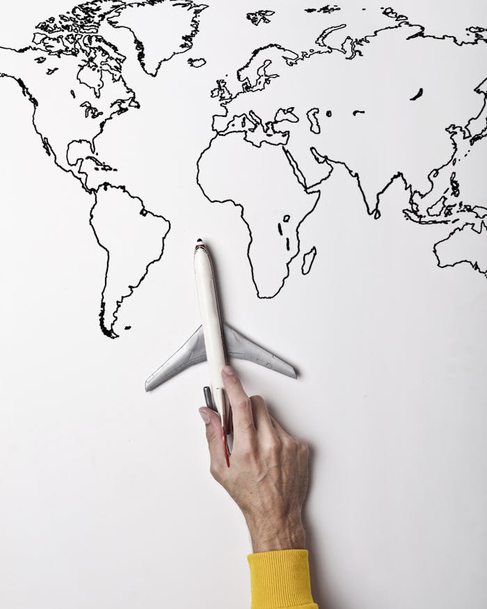 creative-02 Crop person in vibrant yellow clothes holding little gray plane against contour map on white wall as concept of tourism and adventure