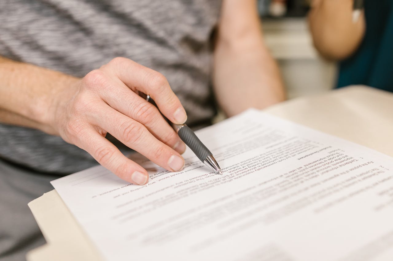 Services-03 Close-up of a person's hand signing an important legal document with a pen indoors.